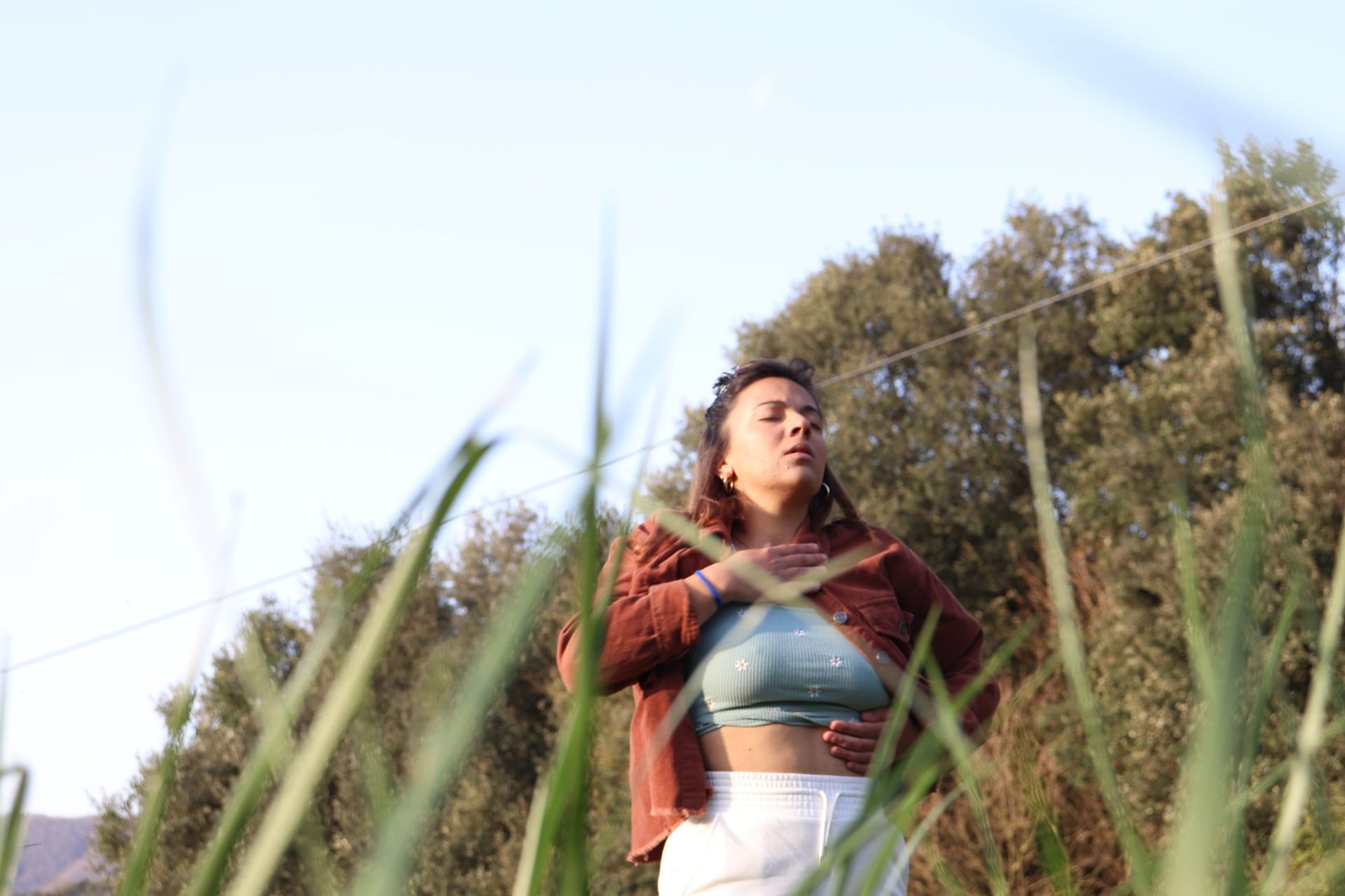 A woman among reeds, eyes closed, arms crossed over her chest, in golden light